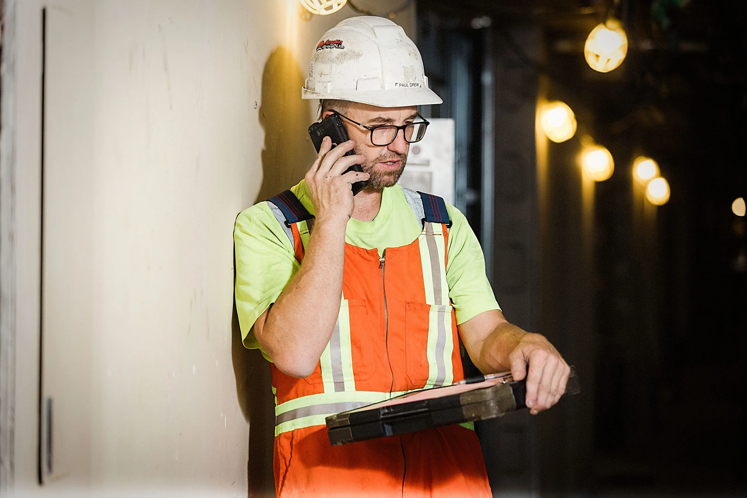 A photo of a construction worker holding a clipboard on a phone call